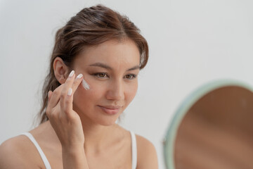 Beautiful Asian woman sit in front of a mirror. face of a healthy woman applying cream and makeup....