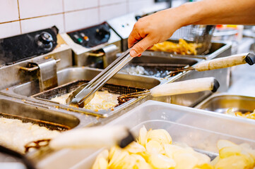 Chef cooking delicious potato chips in hot oil on kitchen