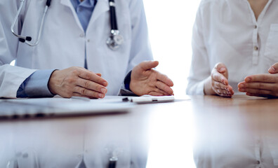 Doctor and patient discussing something while sitting near each other at the wooden desk in clinic. Medicine concept
