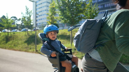 Mother riding bicycle with little boy sitting on back seat