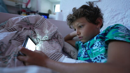 Fototapeta premium One addicted child staring at cellphone screen in the morning bed
