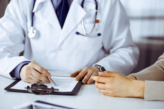 Unknown male doctor and patient woman discussing something while sitting in clinic and using clipboard. Best medical service in hospital, medicine, pandemic stop