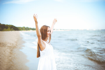 Fototapeta na wymiar Happy smiling woman in free happiness bliss on ocean beach standing with raising hands. Portrait of a multicultural female model in white summer dress enjoying nature during travel holidays vacation