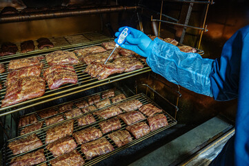 Grilled barbecue pork ribs in a smoker at the factory. The concept of a delicious snack for a...