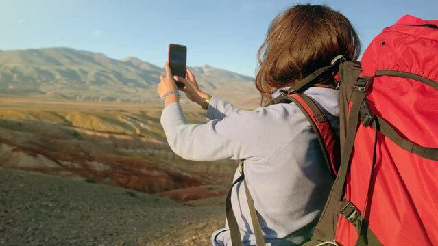 Woman hiker on top of the mountain takes a photo. Female traveler takes a photo on a modern smartphone, makes beautiful pictures of beautiful mountain landscapes. mountain climbing and adventure.