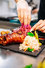 chef hand cooking Baked Pork knuckle with vegetables on plate in kitchen