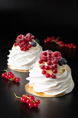 Mini Pavlova cake with raspberry, blueberry and red currant on black background