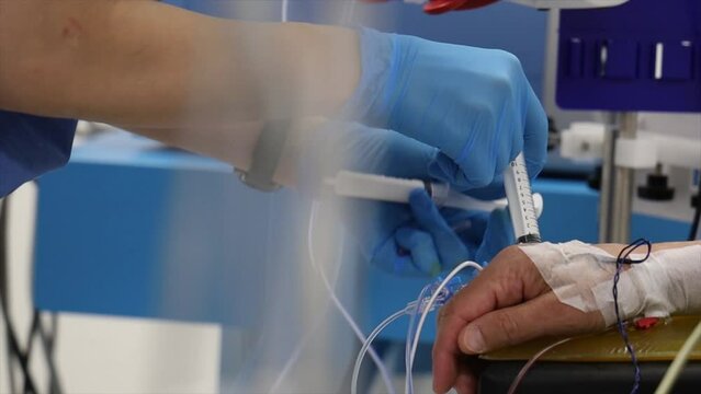 4K close up scene of nurse injecting medicine to patient's IV drip. Patient bandaged hand and nurse hands seen in glow stock video.
