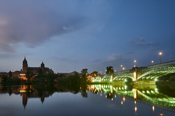 Cathedral of Salamanca at night and Enrique Esteban Bridge view from the Tormes River, Salamanca City. - obrazy, fototapety, plakaty