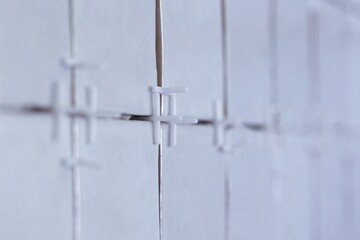 A portrait of white plastic joint spacers placed in the juncture of a recently tiled wall to preserve the distance so the ceramic tiles are installed in a nice pattern.
