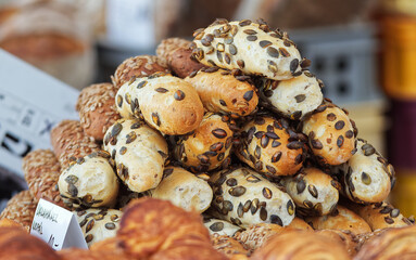 Bakery stall at the farmers market, freshly baked French-style bread with seed sprinkles arranged in a pyramid. Closeup, no people.