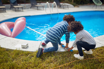 Two little african american kids playing by the pool, cleaning with net, bonding together. Sister and brother together outdoors