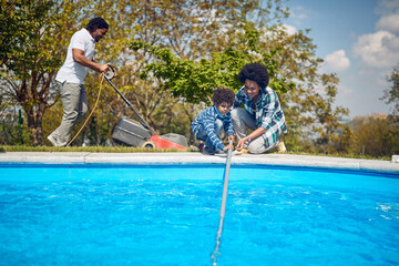 Mother and Son Clean the Pool while Father Tends to the Lawn