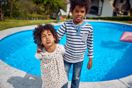 Young children by the pool, african american borther and sister acting silly making faces together standing by the pool outdoors.