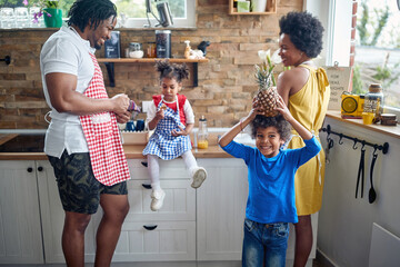 Beautiful joyful family in a domestic kitchen together, little boy holding pineapple over his head...