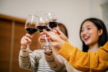 Cheerful friends enjoying home Birthday holiday party. Asian Friends cheering drinking red wine celebrating Christmas or New Year party