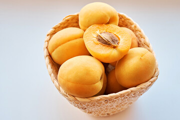 Half of an apricot lie among other apricots in a wicker basket on a white background. Side view. Close-up