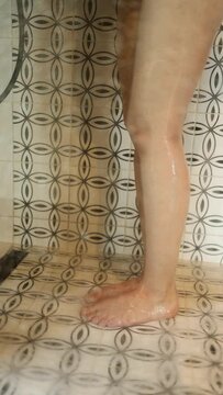 female legs in the shower. water runs down the girl's bare legs in the shower at home. vertical video