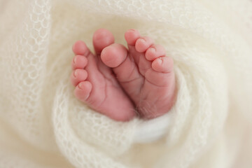 The tiny foot of a newborn baby. Soft feet of a new born in a white wool blanket. Close up of toes, heels and feet of a newborn. Knitted white heart in the legs of a baby. Macro photography.