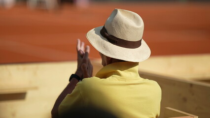 Spectator watching tennis match game clapping hands cheering from stadium seat wearing panama hat