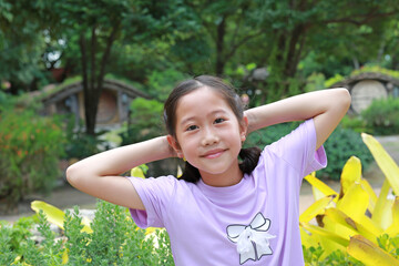 Portrait of Asian girl in casual looking at camera with hands behind head while in the garden.