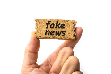 Fake news sign on a piece of wood between fingers