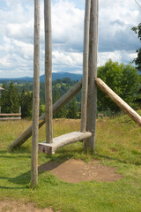 Fototapeta na wymiar A wooden swing for sitting and enjoying the mountain view in the cloudy summer day.
