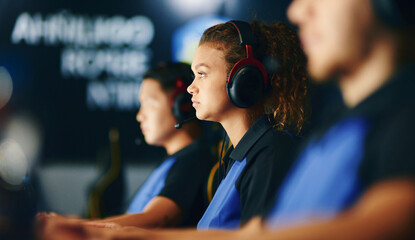 Side view of a focused mixed race girl, female cybersport gamer wearing headphones playing online...