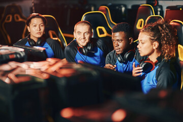 Professional multiracial cybersport team sitting together in gaming club or internet cafe, looking at PC screens while participating in eSport tournament