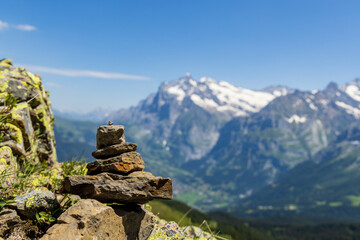 Fototapeta na wymiar A small rock cairn balances on a boulder with a view of mountains of the Swiss alps and blue skies in the background