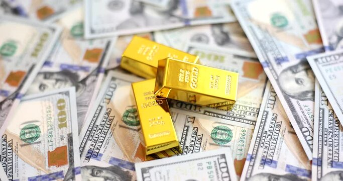 Gold ingots lie on scattered dollars, a close-up, slowmotion. Capital saving in crisis times, investment