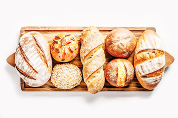 Bakery - various kinds of breadstuff. Bread rolls, baguette, sweet bun and croissant on wooden board on white background. Flat lay