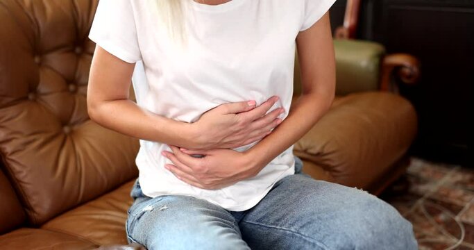 A woman at home on the couch strokes the stomach close-up. Abdominal pain, colic in the intestines, slowmotion