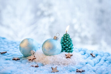 Christmas products background. Blue frosty pattern baubles on snow with green spruce tree shape candle burning. Bokeh snowy winter forest background.