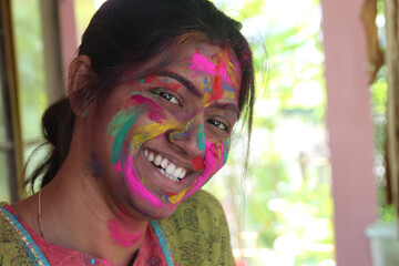 An Indian lady in 30s with face full of vibrant colours and looking towards the camera and smiling
