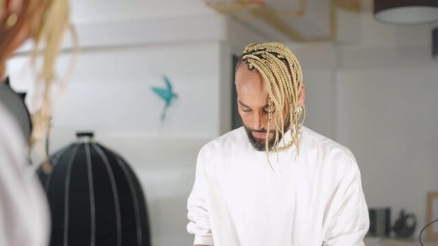 Attractive stylish black gay man in white look at mirror view from behind. Lifestyle lgbtq pride concept. Feminine man with beard and makeup on face straightens clothes in front of mirror