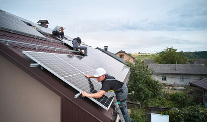 Men technicians mounting photovoltaic solar moduls on roof of house. Workmen in helmets installing solar panel system outdoors. Concept of alternative and renewable energy. Aerial view.