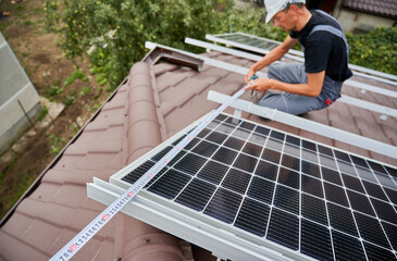 Man measuring photovoltaic solar panels with tape measure. Male worker taking measurements before mounting solar modules on roof of house for generating electricity through photovoltaic effect.