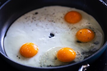 A portrait of multiple sunny side up eggs baking in a frying pan. The cook is creating a great breakfast, lunch or brunch. The egg white and the yolk is nicely separated.