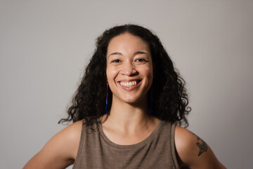 A multiracial woman with long, curly hair smiles for a studio portrait. She look cheerful, confident, and approachable. Adding backstory, she is LGBTQ and proud.