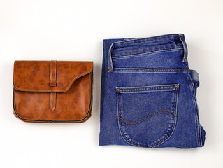 Jeans and a small leather handbag on a white background. Flat lay casual wear. Blue classic jeans, small brown clasp bag.