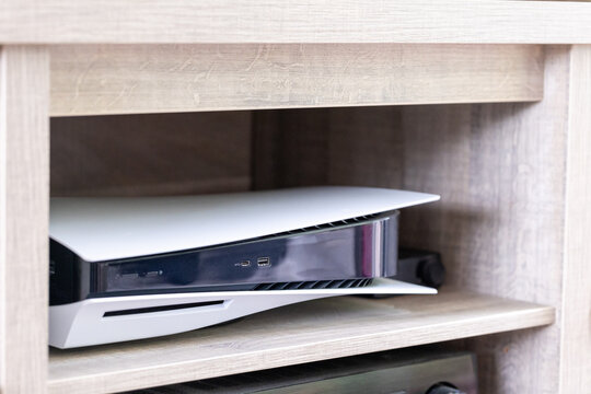 Brecht, Belgium - 14 july 2023: A portrait of a standard black and black playstation 5 console with a disc drive and usb ports standing in a tv cabinet ready to play PS5 video games.