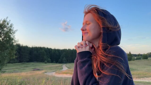 young cute woman dreaming and praying outdoors at sunset or sunrise in the park