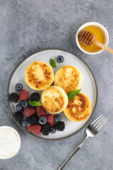 Cottage cheese pancakes, syrniki with sour cream, honey, berries on blue background. Top view. Russian, ukrainian food