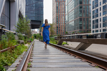 A woman in blue maxi dress walking on an old railing turned into a pathway - the famous High Line...