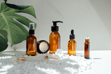 Amber bottles with facial treatment on a yellow table with green leaves on backdrop. Front view