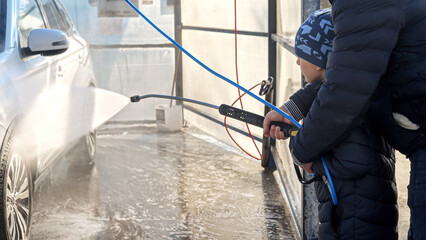 Little son with father using water jet to wash and clean car at outdoor self service car wash