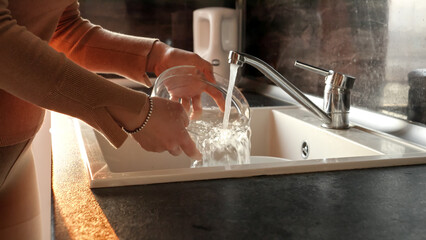 Closeup of female hands washing glass bowl in kitchen sink. Housewife working, domestic chores,...