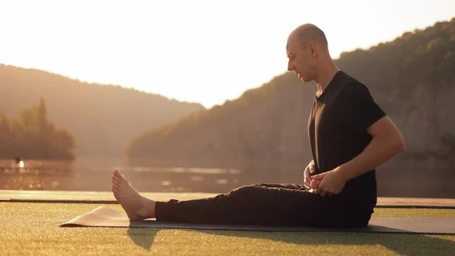 Young happy guy doing yoga outdoors in the morning on the river bank. Meditation. An active healthy lifestyle in peaceful nature. Improving awareness.