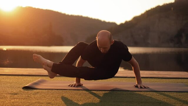 Man doing Ashtavakrasana power balance pose outdoors. The master of yoga exercises a handstand on. piers by the river at dawn.